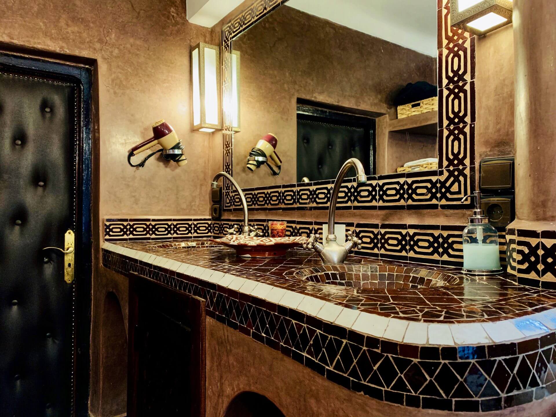 Waschbecken aus dunklem Mosaik und einem großem Spiegel