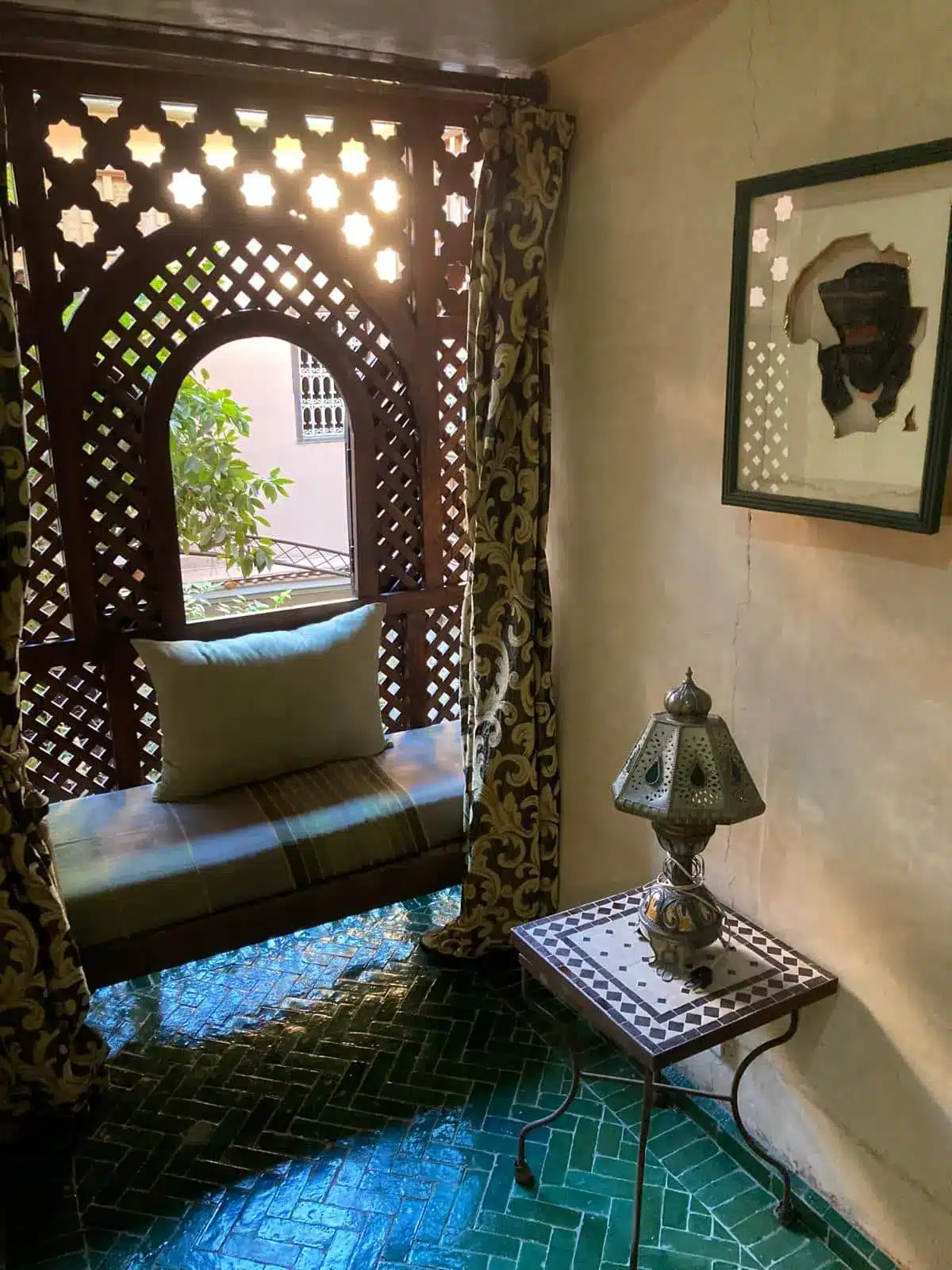 Privater Balkon des Zimmers Assalam im Riad La Maison Nomade mit traditioneller Sitzbank und Blick in den grünen Innenhof.